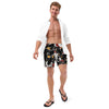 Man wearing a white shirt over black swim trunks with colorful black panther tattoo heads designs on a white background