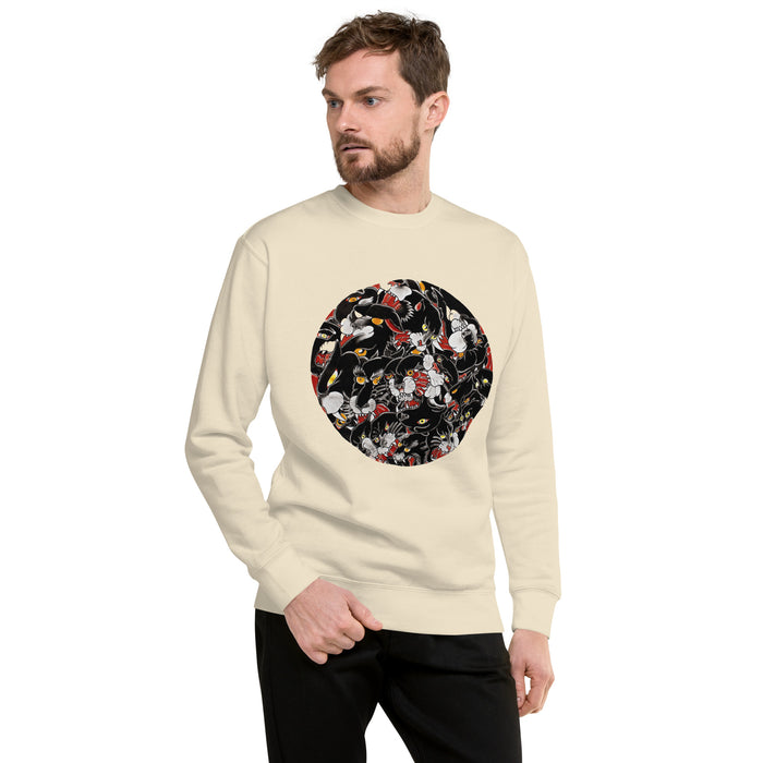 A man wearing a cream-colored crewneck sweatshirt with a circular graphic on the chest of tattoo style panther heads paired with black pants, set against a plain white background