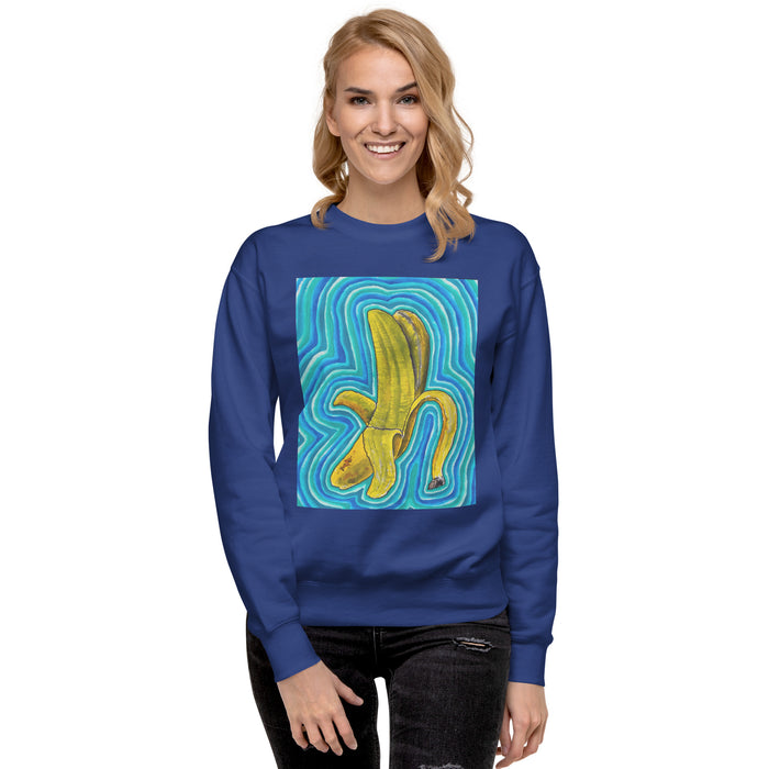 A woman wearing a royal blue crewneck sweatshirt with a graphic print of a yellow banana on a swirling blue and green background, paired with black jeans, against a plain white studio background.