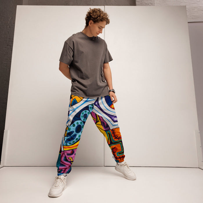 A man modeling colorful patterned jogger pants with a dark gray t-shirt and white sneakers, standing in front of a white studio backdrop.