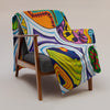 Colorful, psychedelic, abstract patterned blanket on a gray sofa in a modern living room.