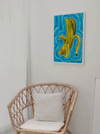 psychedelic banana painting radiating waves of blue, turquoise, and green energy bands in a visionary art style hanging on a wall by a rattan chair