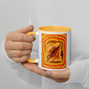 A person in a white long-sleeve shirt holds a white ceramic mug with a yellow interior and handle. The mug features a colorful graphic print of a toasted slice of bread with a diagonal cut, surrounded by concentric orange and yellow rings.