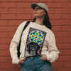 a beige long sleeve t-shirt with a chimp face  in front of a green and yellow circular mandala and a psychedelic geometric background of reds and whites.