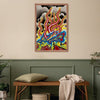 A framed abstract painting featuring vibrant red, yellow, blue, and black flame-like patterns hangs on a beige wall above a green wainscoted bench with a pillow and throw blanket.