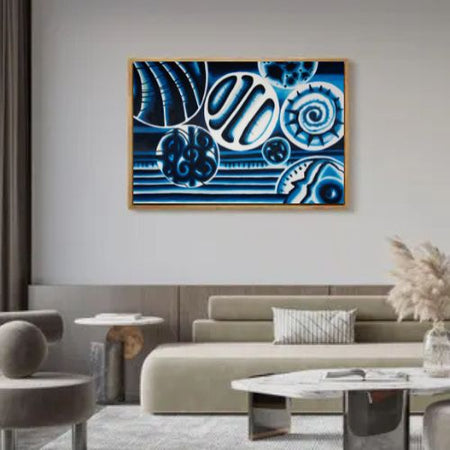 A framed abstract canvas print featuring blue and white organic patterns, displayed on a light gray wall above a modern beige sofa in a styled living room.