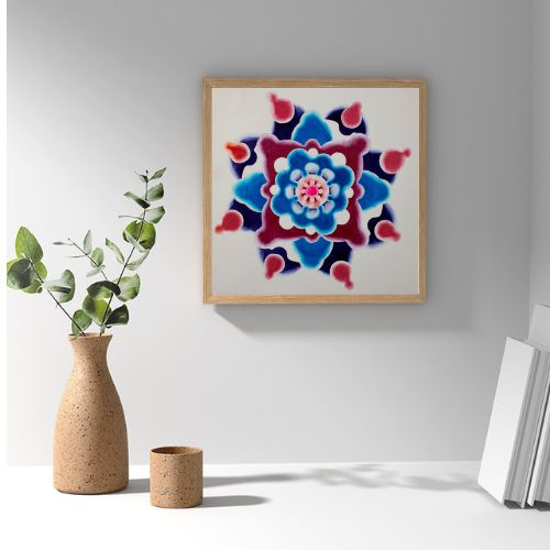 A square framed wall art print featuring a colorful mandala design in shades of blue, red, and pink on a white background, styled on a white shelf next to a vase with greenery and books.