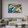 A colorful abstract framed wall art print hangs above a beige sofa in a modern living room setting. The artwork features bold, flowing shapes in blue, yellow, purple, and green.