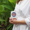 woman white stainless steel wine tumbler with an abstract floral mandala in reds and blues in front of greenery