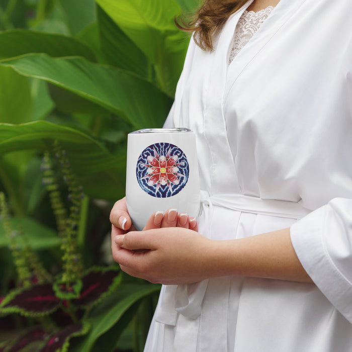 woman white stainless steel wine tumbler with an abstract floral mandala in reds and blues in front of greenery
