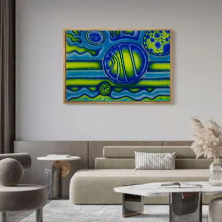 A framed abstract art print featuring vibrant blue and green organic patterns, displayed on a light gray wall above a modern beige sofa in a styled living room.