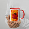 hands holding a white and red coffee cup with a tomato with radiating red and yellow striped around it.