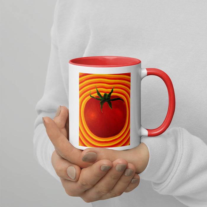 hands holding a white and red coffee cup with a tomato with radiating red and yellow striped around it.
